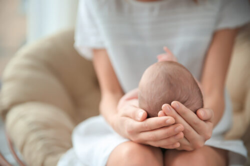 Mother holding cute newborn baby girl, indoors